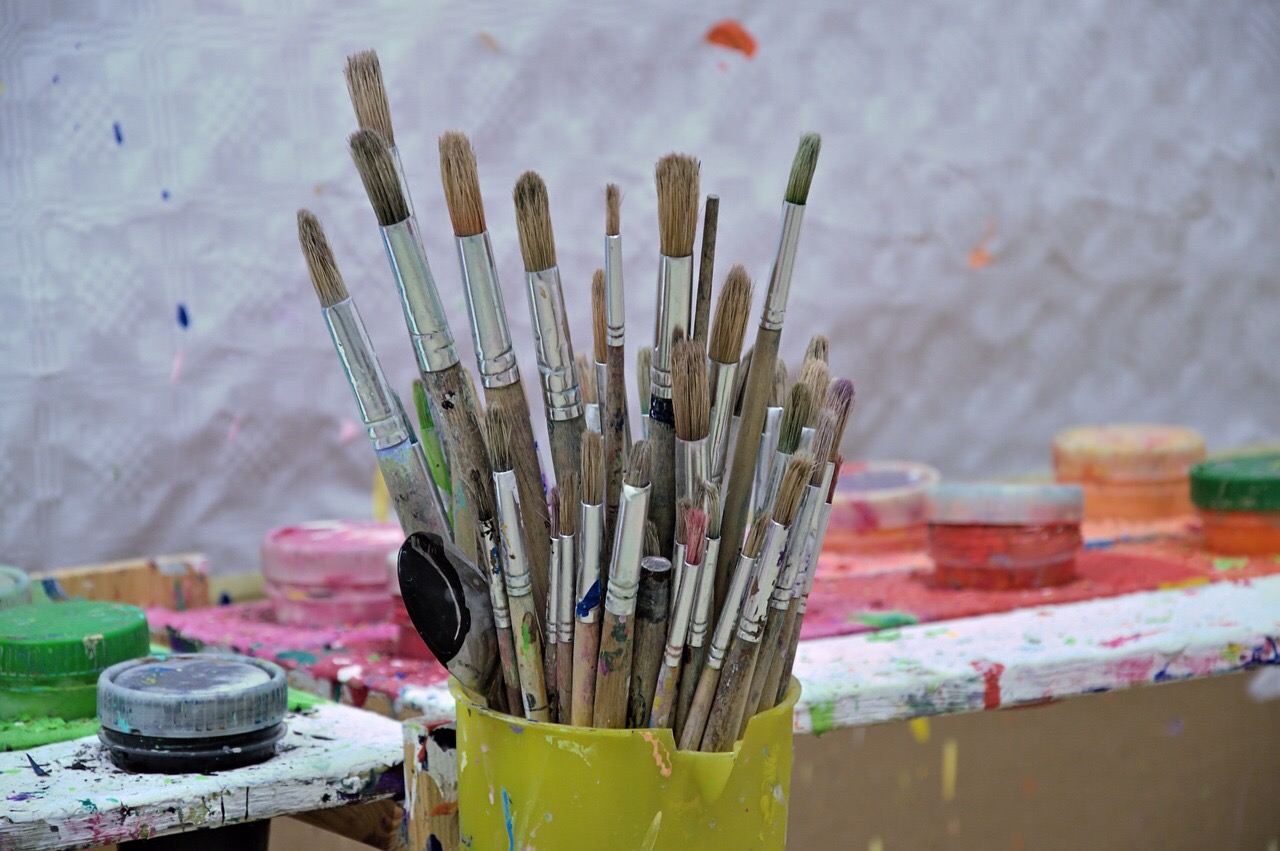 Yellow coffee mug with many paint brushes sticking up from it. Background has paint here and there on surfaces. ti ... Arts and Crafts Activities