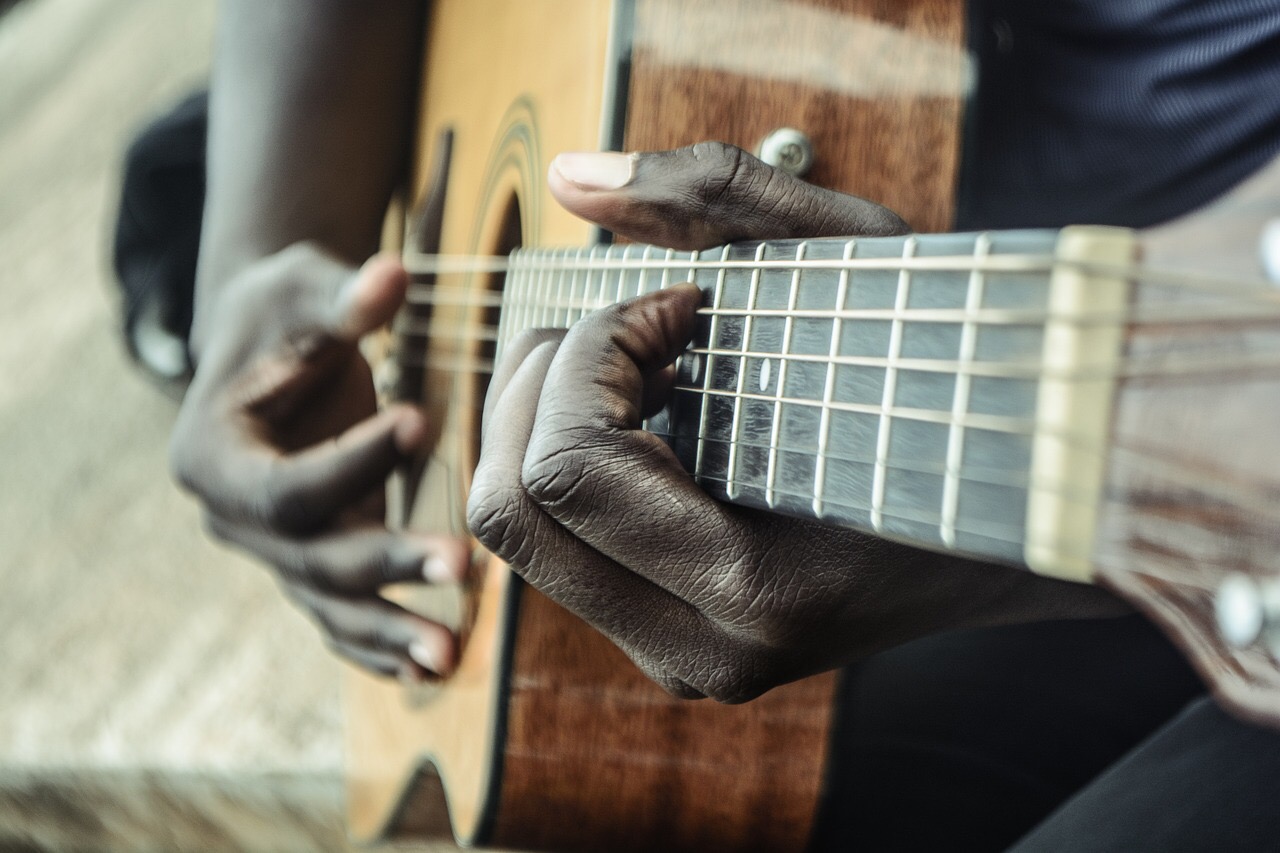 Close-up of acoustic guitar played by hands of African-American man. Represents Acrican-Americans, Black history, and/or music. Credit: sycline/Pixabay